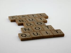 Wooden Scrabble tiles arranged to spell 'Fail but do not quit,' inspiring determination.