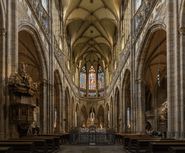 Interior of a Gothic church in Prague showcasing stained glass windows and vaulted ceilings.