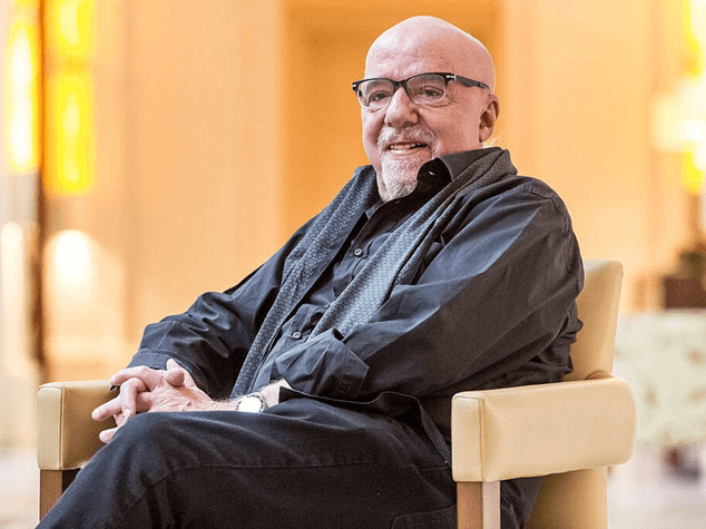 Paulo Coelho, Brazilian author of "The Alchemist," seated comfortably in an indoor setting.