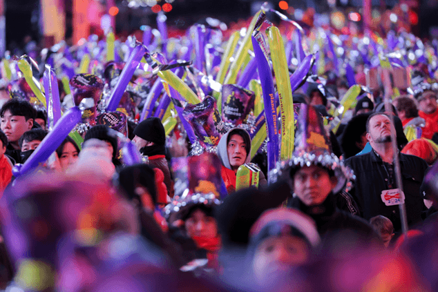 Crowd celebrating New Year's Eve with colorful noise sticks and festive hats at Times Square Ball Drop event
