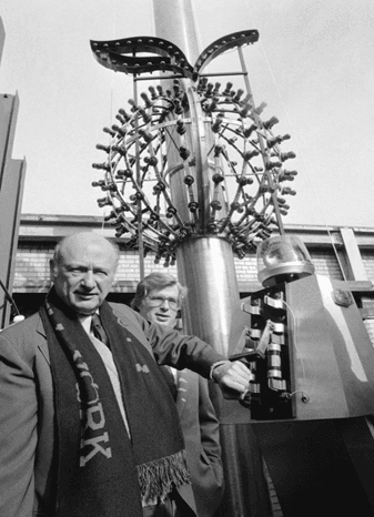 Early Times Square ball drop device with man posing by control panel in black and white historical photo.