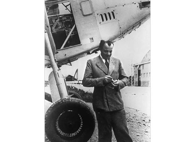 Antoine de Saint-Exupéry standing beside a vintage airplane, highlighting his background as a pioneering aviator.