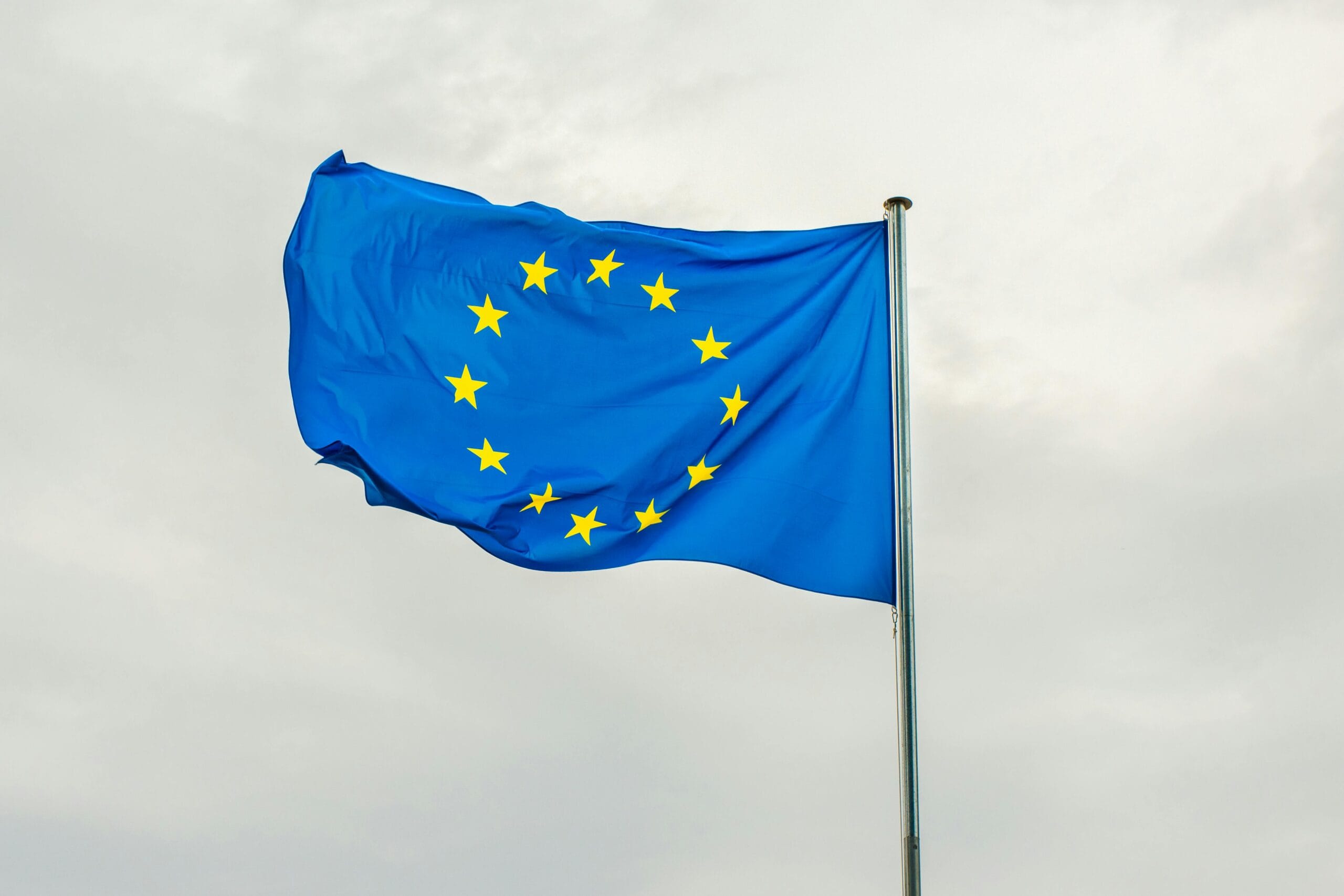 The European Union flag gracefully waving on a flagpole against a cloudy sky.
