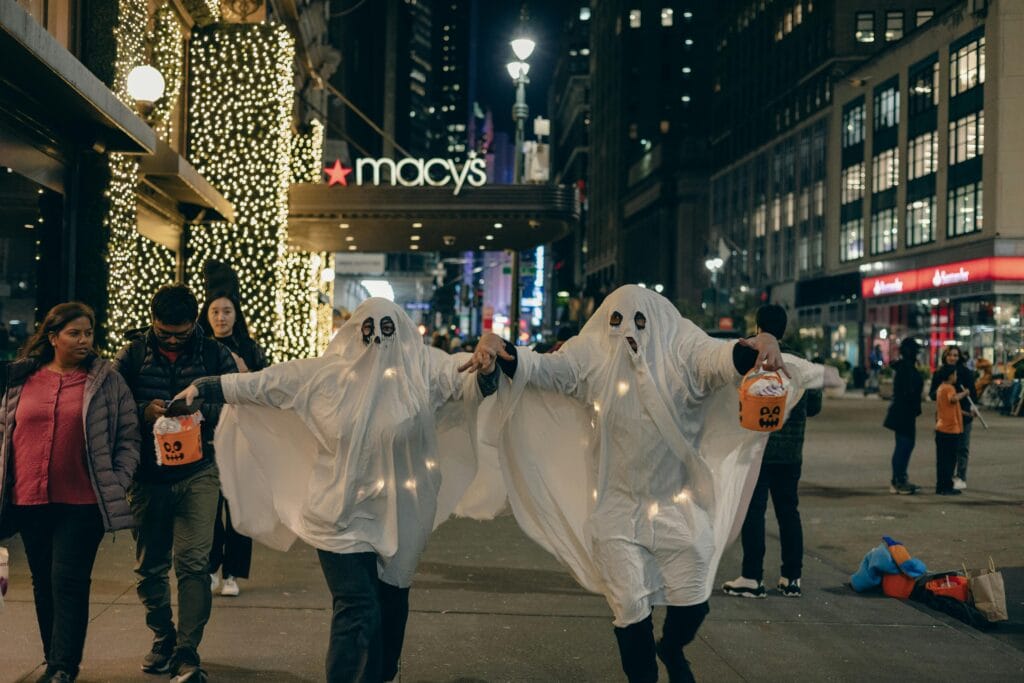 Adults in ghost costumes walk in New York City at night, celebrating Halloween.
